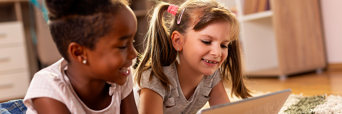 Two young girls smiling as they look at a tablet