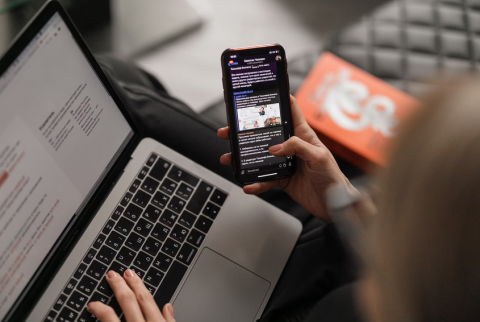 close up of someone holding their phone while also looking at their laptop