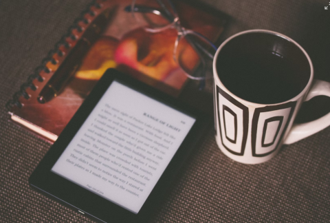 photo of a kindle on top of notebook next to cup of coffee or tea