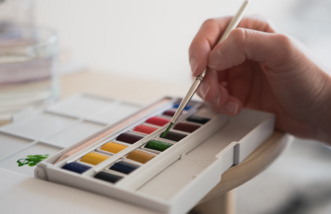 close up of a hand putting a brush onto a watercolor palette