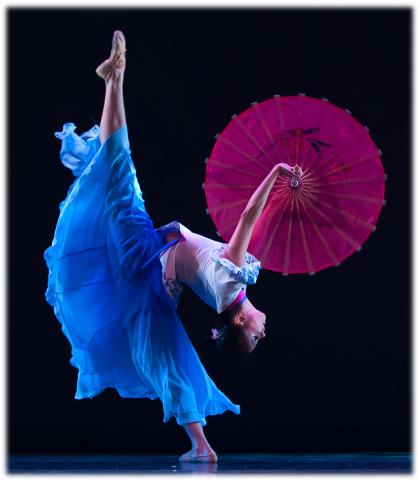 Female dancer with leg in air and holding pink fan umbrella