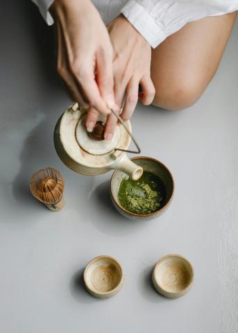 A person's hands holding a teapot, pouring water into a teacup
