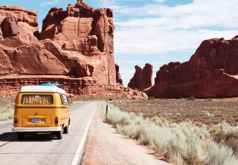 photo of a yellow van driving down a desert road with buttes in the distance