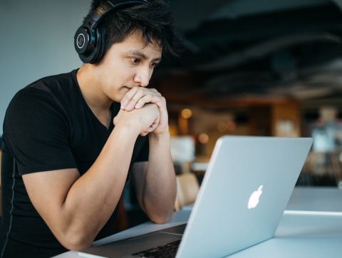 photo of a masculine person staring at a laptop while wearing over-the-ear headphones