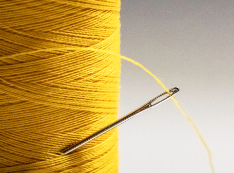 photo of a needle stuck into a spool of yellow thread
