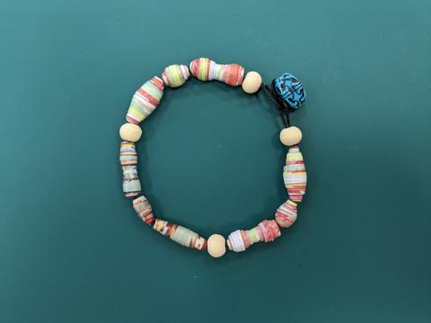 multicolor paper bead bracelet laying on a green mat