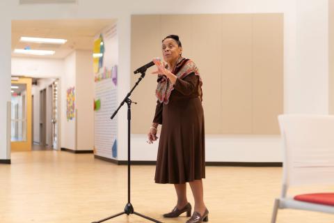 Actress and Storyteller, Jean Donatto, stands in front of a microphone sharing the history to life by stepping into the role of Rosa Parks.
