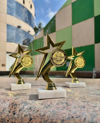 3 trophies are displayed in front of a colorful background