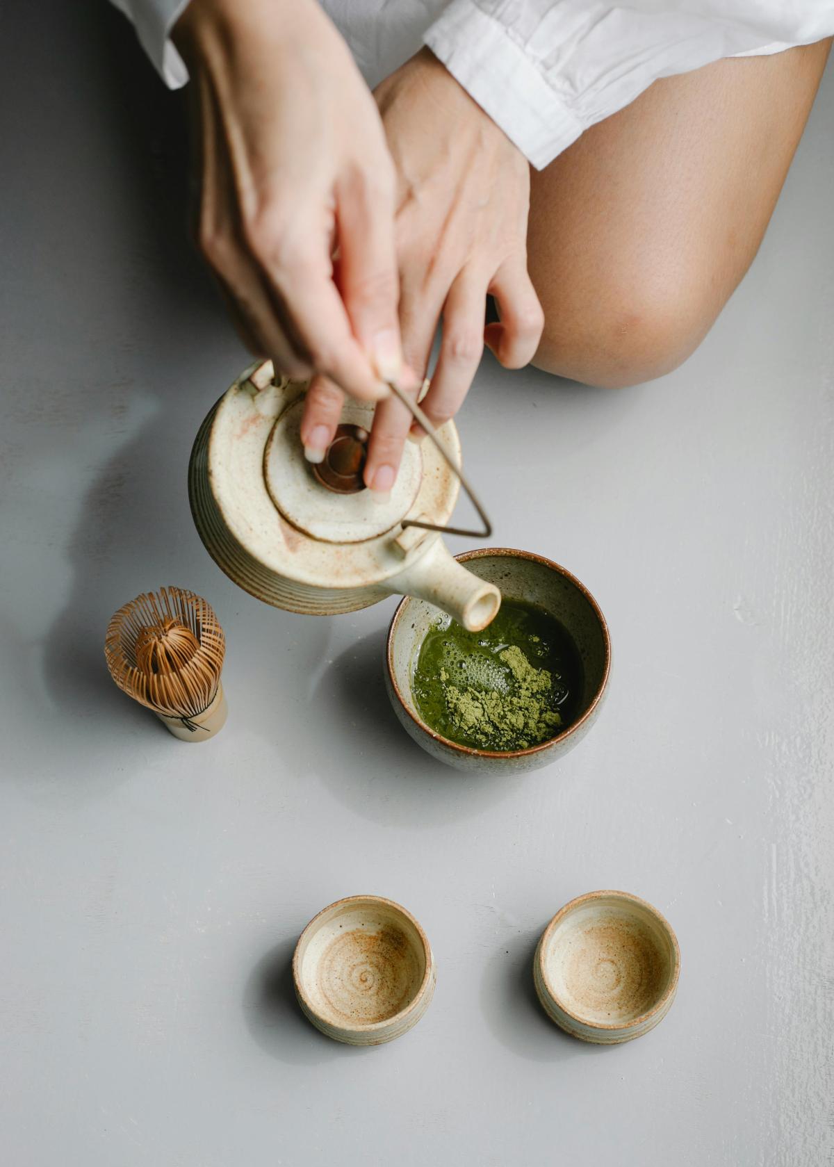 A person's hands holding a teapot, pouring water into a teacup