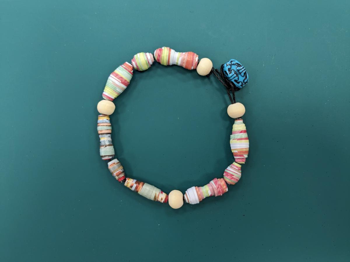 multicolor paper bead bracelet laying on a green mat
