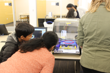 Mother and son leaning forward to watch the 3D printer print an object inside the library