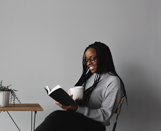 Woman smiling while reading a book with a mug in her other hand