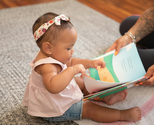 Baby girl turning the pages of a picture book that her parent is holding in front of her