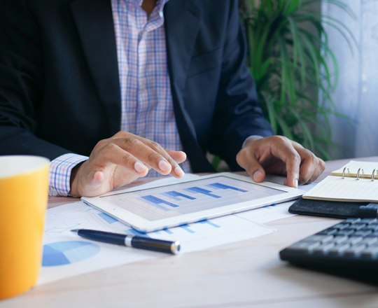 Man sitting at a desk and looking at a tablet with bar graphs 