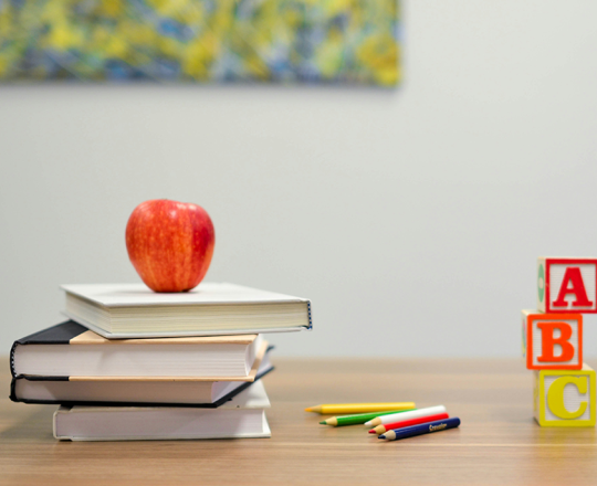 A group of objects on a desk: an apple sitting on top of a stack of books, pencils, and wooden ABC blocks