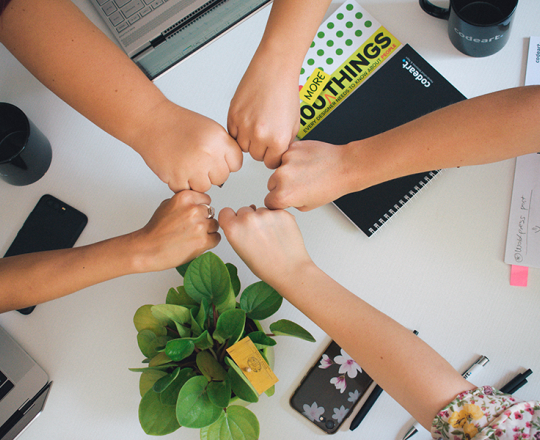Group of five teens putting their fists together over a desk