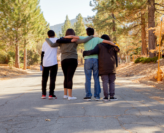 Group of four teens with arms around each other with their back to the camera