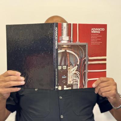 Efrain DeLeon holding up a reference book about Advanced Wiring